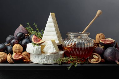 Siyah arka planda meyveli yumuşak peynirler. İncirli, üzümlü, cevizli, ballı ve kekikli Camembert peyniri..