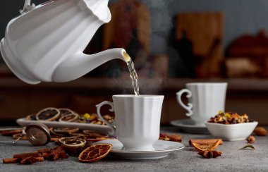 Eski bir taş masanın üzerinde malzemelerle birlikte bitki çayı. Bitki çayı bir fincana doldurulur..