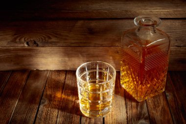 Zarif viski bardağı ve kehribar sıvısıyla dolu sürahi eski bir ahşap masada. Boşluğu kopyala.