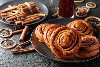 Kanelbullar - İsveç tarçınlı çörekler ya da dürümler. Siyah taş bir masada taze pişmiş çörekler..