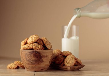 Yulaf ezmeli kurabiye ve süt mutfak masasında. Süt şişeden bardağa dökülür. Kopyalama alanı olan bej arkaplan.