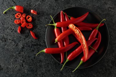 Siyah taş bir masada yeşil saplı taze kırmızı biber. Üst görünüm, alanı kopyala.