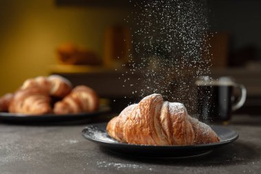 Taze kruvasan ve mutfak masasında sade kahve. Şeker tozu serpiştirilmiş kruvasanlar. Seçici odak.