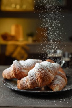 Taze kruvasan ve mutfak masasında sade kahve. Şeker tozu serpiştirilmiş kruvasanlar. Seçici odak.