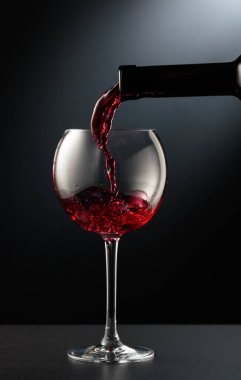 Kırmızı şarabı siyah arka planda bir şarap bardağına döküyorum..