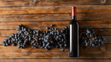 Eski ahşap bir masada mavi üzümler ve bir şişe kırmızı şarap. Üst Manzara. Boşluğu kopyala.