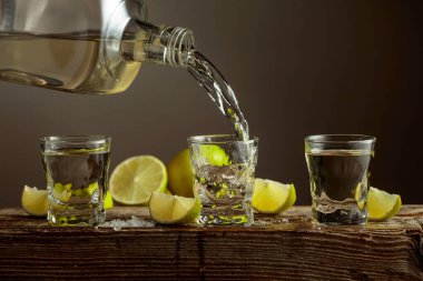 Eski ahşap bir tahtanın üzerinde tuz ve limon dilimli altın tekila. Tekila şişeden bardağa dökülür..