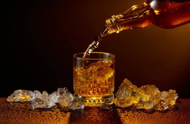 Viski şişeden cama doluyor. Viski ve buz, siyah ıslak bir masada. Sarı ışık, boşluğu kopyala.