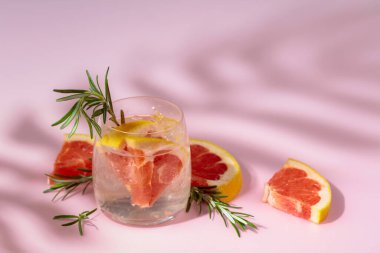 Buzlu, greyfurtlu ve biberiyeli yaz içeceği. Serin, gevrek ve pembe arka planda palmiye gölgeleri tarafından öpülmüş. Boşluğu kopyala.