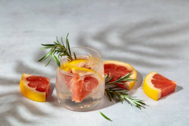 Buzlu, greyfurtlu ve biberiyeli ferahlatıcı bir yaz içeceği. Serin ve ferahlatıcı bir içecek, mermer bir masanın üzerinde palmiye gölgeleri. Boşluğu kopyala.