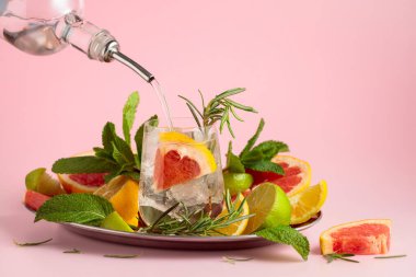 Buzlu, narenciyeli, biberiyeli ve naneli kokteyl. Cin veya rom şişeden bardağa dökülür. Kopya alanı ile pembe arkaplan.