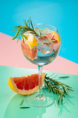 Yaz kokteylini cin, tonik, greyfurt ve biberiyeyle tazeliyorum. Buzda servis ediliyor, renk ve tazelikle dolup taşıyor. Parlak renkli arkaplan.
