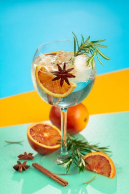 Cin, tonik, kan portakalı, tarçın, anason ve biberiyeli yaz kokteyli. Buzda servis ediliyor, renk ve tazelikle dolup taşıyor. Parlak renkli arkaplan.