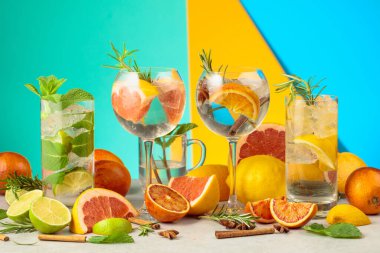 Beyaz mermer bir masada malzemelerle yaz kokteyllerini tazeliyorum. Mojito ve çeşitli cin tonik kokteylleri parlak renkli bir arka planda..