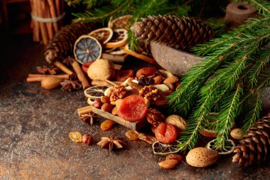Kahverengi bir arka planda kurumuş meyve ve fındık. Kurutulmuş turunçgiller, kayısılar, kuru üzümler, çeşitli fındıklar, tarçın çubukları ve anason içeren bir Noel..