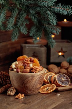 Eski ahşap bir masada kurumuş meyve ve çeşitli fındıklar. Noel 'de ladin dalları ve eski fenerlerde yanan mumlar.