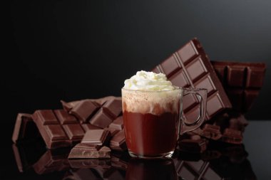 Krem şantili sıcak çikolata. Arka planda kırık bir çikolata parçasında. Kopyalama alanı olan siyah yansıtıcı arkaplan.