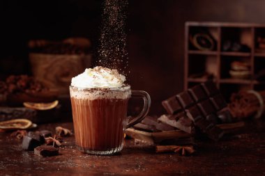 Üzerine krem şanti ve çikolata parçacıkları serpiştirilmiş sıcak çikolata. Eskimiş kahverengi arka planda yer alan malzemeler içeren bir çikolata içeceği..