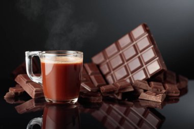 Bir bardak sıcak çikolata ve kırık acı çikolata. Kopyalama alanı olan siyah yansıtıcı arkaplan.