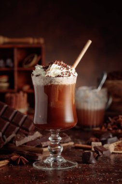 Üzerine krem şanti ve çikolata parçacıkları serpiştirilmiş çikolata içeceği. Eskimiş kahverengi arka planda yer alan malzemeler içeren bir çikolata içeceği..