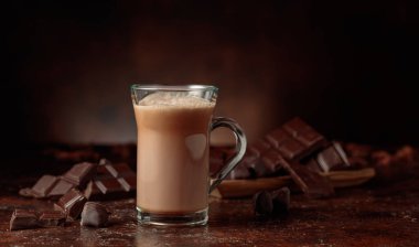 Cam bardakta kakao ve koyu kahverengi arka planda acı çikolata parçaları. Boşluğu kopyala.