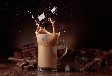 Acı çikolata parçaları cam bardağa dökülür kakao içeceği ile güzel su sıçratır. Boşluğu kopyala.