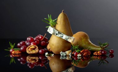 Armut, ceviz, kırmızı üzüm ve biberiyeli mavi peynir. Siyah yansıtıcı arka planda meyveleri olan geleneksel küflü peynir. Boşluğu kopyala.