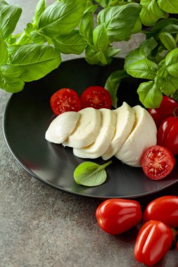 Domatesli Mozzarella peyniri ve siyah tabakta fesleğen..