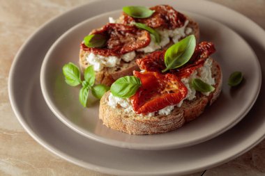 Ciabatta, zeytinyağında kurutulmuş domates, krem peynir ve fesleğen. Bej tabakta geleneksel İtalyan atıştırması..