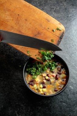 Siyah taş bir masada patates, domates, paprika, havuç ve pastırma ile kırmızı fasulye çorbası. Doğranmış maydanozu çorba kasesine serp..