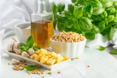 Pesto sosu yapmak için gerekli malzemeler. Fesleğen, çam fıstığı, sarımsak, parmesan ve beyaz ahşap bir masada zeytin yağı. Geleneksel İtalyan pesto tarifi.