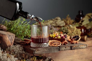 Bitkisel acı likör eski bir şişeden bir bardağa dökülür. Bitkiler, kökler, görünen baharatlar gibi doğal malzemeler. Aromatik kahverengi sıvı ev yapımı bir zanaat olduğunu gösteriyor. Boşluğu kopyala.