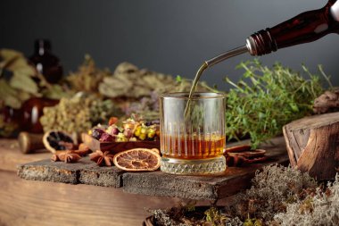 Bitkisel acı likör eski bir şişeden bir bardağa dökülür. Bitkiler, kökler, görünen baharatlar gibi doğal malzemeler. Aromatik kehribar sıvısı ev yapımı bir zanaat olduğunu gösteriyor..