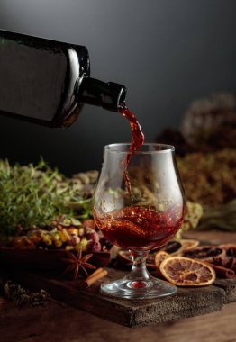 Bitkisel acı likör eski bir şişeden bir bardağa dökülür. Bitkiler, kökler, görünen baharatlar gibi doğal malzemeler. Aromatik kahverengi sıvı ev yapımı bir zanaat olduğunu gösteriyor. Boşluğu kopyala.