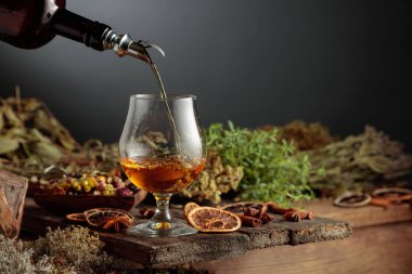 Bitkisel acı likör eski bir şişeden bir bardağa dökülür. Bitkiler, kökler, görünen baharatlar gibi doğal malzemeler. Aromatik kehribar sıvısı ev yapımı bir zanaat olduğunu gösteriyor..