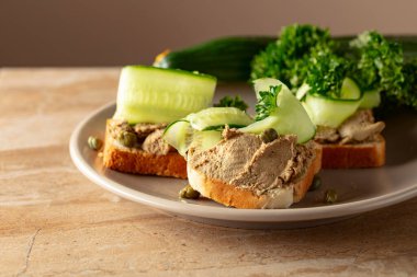 Bej tabakta ezmeli tost. Pate, taze salatalık, kapari ve maydanozlu sandviç..