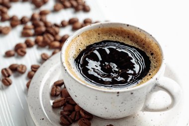 Beyaz ahşap bir masada sade kahve ve kahve çekirdekleri. Bir fincan kahveye bir damla düştü. Boşluğu kopyala.