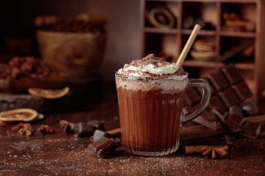 Üzerine krem şanti ve çikolata parçacıkları serpiştirilmiş sıcak çikolata. Eskimiş kahverengi arka planda yer alan malzemeler içeren bir çikolata içeceği..