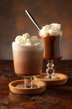 Kremalı sütlü çikolatalı içecekler. Eski kahverengi bir masada krem şantili ev yapımı latte. Boşluğu kopyala.