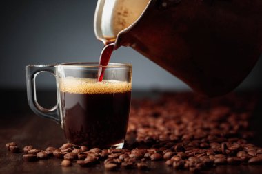 Koyu kahve Türk bakır kahve demliğinden cam fincana dökülüyor.