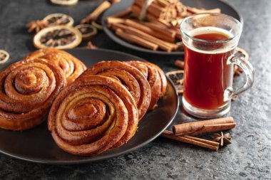 Kanelbullar - Swedish cinnamon buns or rolls. Freshly baked buns on a black stone table. Kanelbullar are more than just Swedish cinnamon buns. Their warm, spicy aroma immediately evokes a feeling of comfort and calm, as if time has slowed down for a