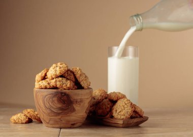 Yulaf ezmeli kurabiye ve süt mutfak masasında. Süt şişeden bardağa dökülür. Kopyalama alanı olan bej arkaplan.