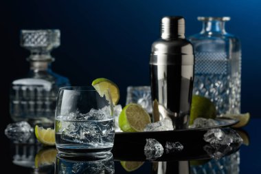 Buzlu bir bardakta votka veya cin. Siyah yansıtıcı arka planda ezilmiş buz ve limon dilimleri.
