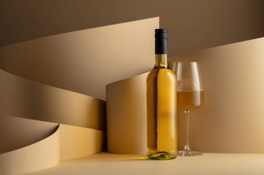 Bottle and glass of white wine on a beige background. Copy space.