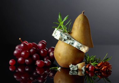 Armut, ceviz, kırmızı üzüm ve biberiyeli Gorgonzola. Siyah yansıtıcı arka planda meyveleri olan geleneksel küflü peynir. Boşluğu kopyala.