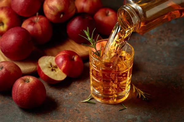 Apple kombucha şişeden bardağa dökülür. Bir bardak kombu çayı ve taze elmalar eski bir mutfak masasında oturur..