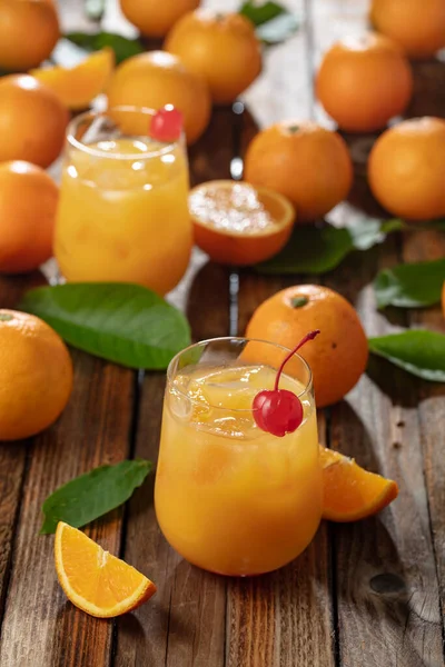 Kırmızı kirazla süslenmiş portakal suyu. Buzlu ve taze meyveli bir içecek eski bir ahşap masada..