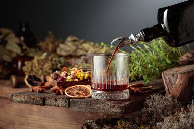 Bitkisel acı likör eski bir şişeden bir bardağa dökülür. Bitkiler, kökler, görünen baharatlar gibi doğal malzemeler. Aromatik kahverengi sıvı ev yapımı bir zanaat olduğunu gösteriyor. Boşluğu kopyala.