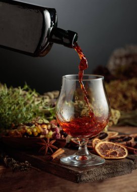 Bitkisel acı likör eski bir şişeden bir bardağa dökülür. Bitkiler, kökler, görünen baharatlar gibi doğal malzemeler. Aromatik kahverengi sıvı ev yapımı bir zanaat olduğunu gösteriyor. Boşluğu kopyala.