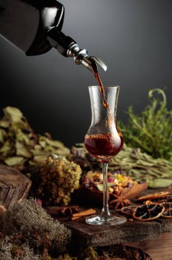 Bitkisel acı likör eski bir şişeden bir bardağa dökülür. Bitkiler, kökler, görünen baharatlar gibi doğal malzemeler. Aromatik kahverengi sıvı ev yapımı bir zanaat olduğunu gösteriyor..